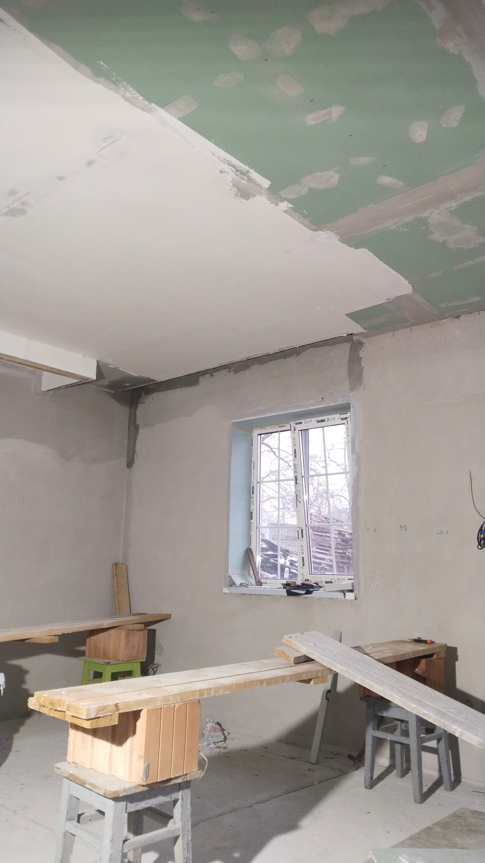 На фото видно процесс отделки стен: шпаклевка потолка, грунтовка и шпатлевка стыков гипсокартона для выравнивания поверхностей.