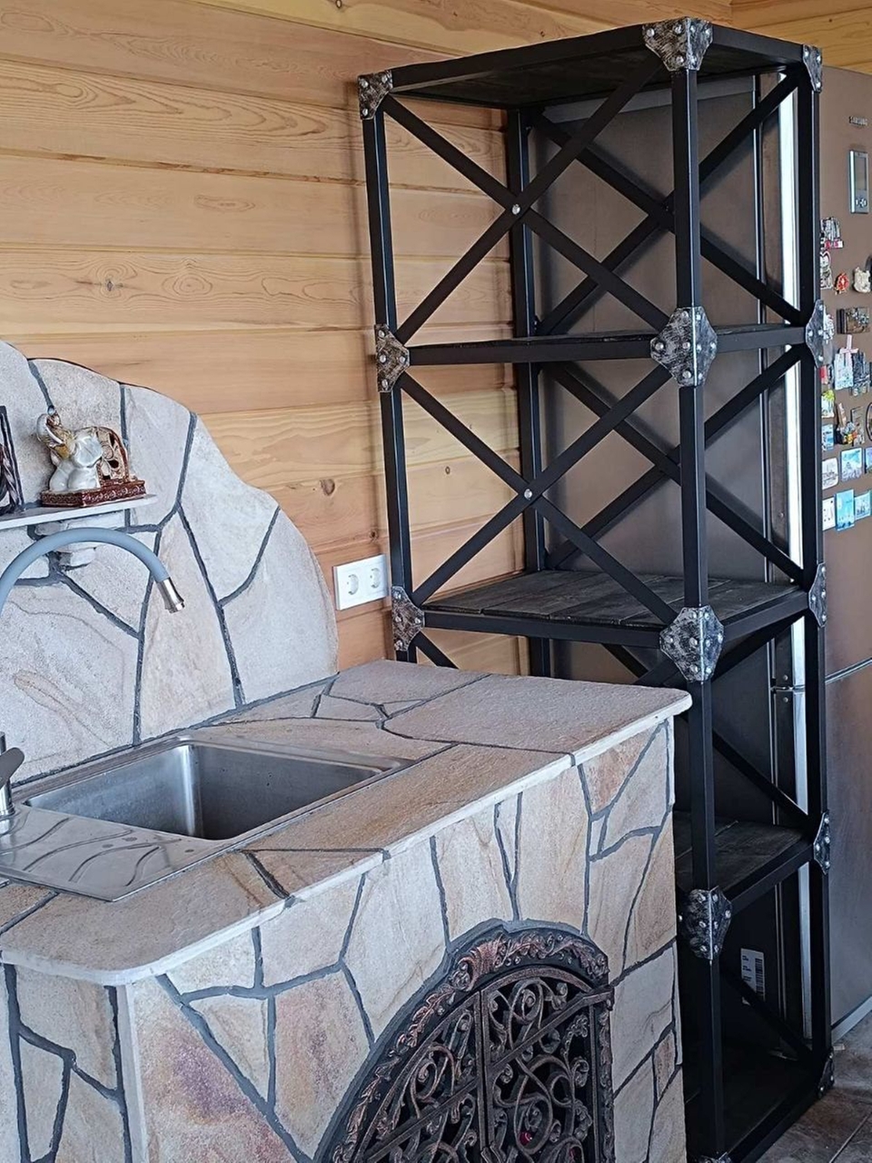 Уличный барбекю комплекс: Кирпичный мангал с плиточной облицовкой и металлический каркас для хранения дров и аксессуаров.
Функциональность и удобство: Встроенная мойка и столешница из камня обеспечивают комфорт при готовке на открытом воздухе.