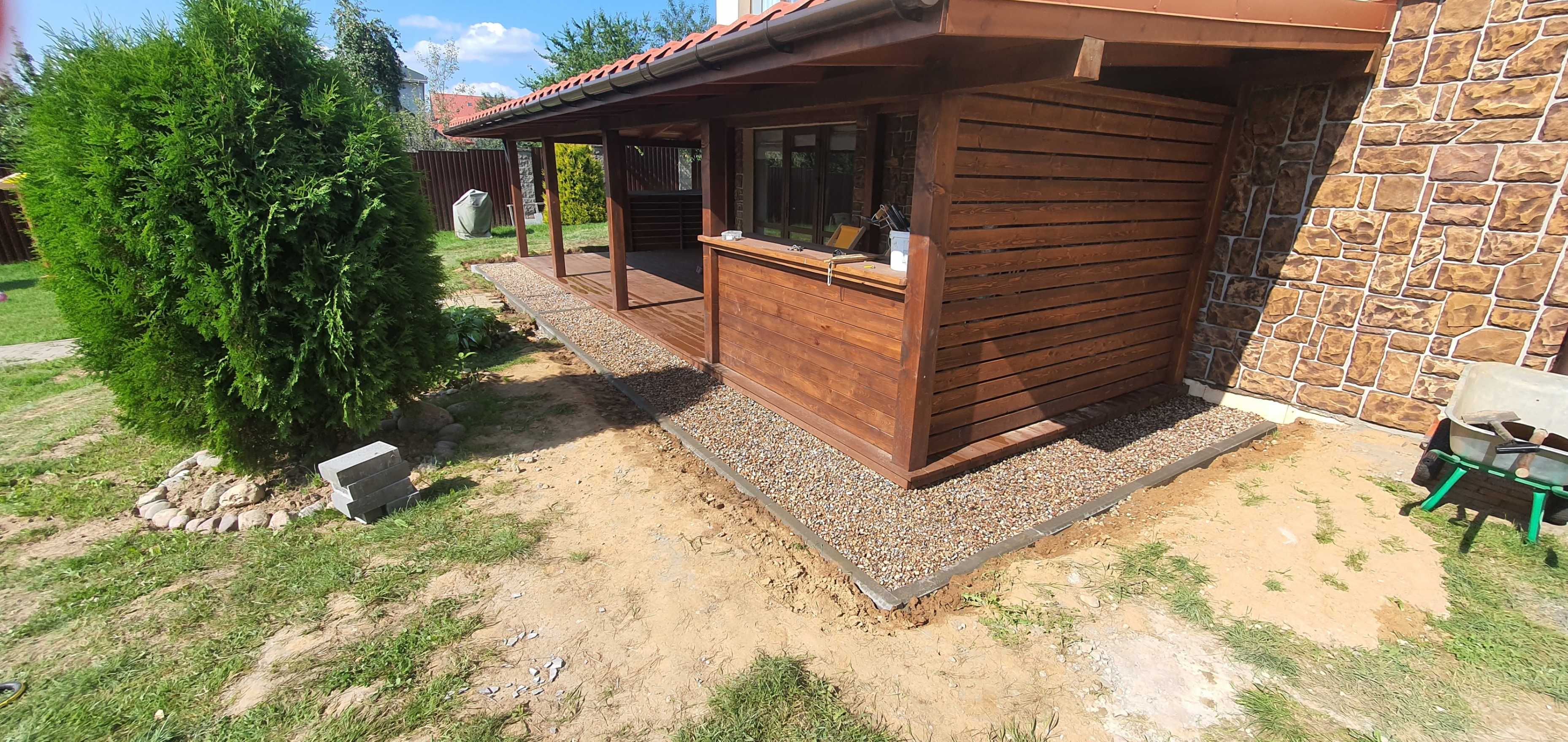 На фото готовая терраса, выполненная под ключ: отделка натуральной деревянной обшивкой. Водосточная система установлена для защиты от осадков, а отмостка вокруг террасы обеспечивает дополнительную защиту фундамента от влаги и продлевает срок службы.