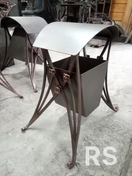 Кованая урна для лавочки: компактная, стильная, выполнена из прочного металла с антикоррозийным покрытием.
Использованы техника художественной ковки, сварка и обработка для защиты от погодных условий.